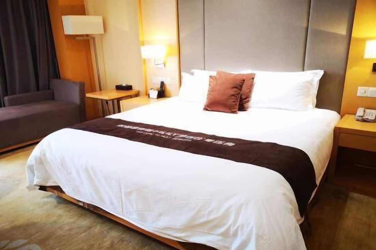 Hotellihuone, jossa on suuri sänky, yöpöytä, lamppu ja tuoli.