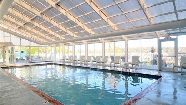 Ein überdachter Schwimmbereich mit klaren Glaswänden, gefliestem Boden und Liegestühlen am Pool.