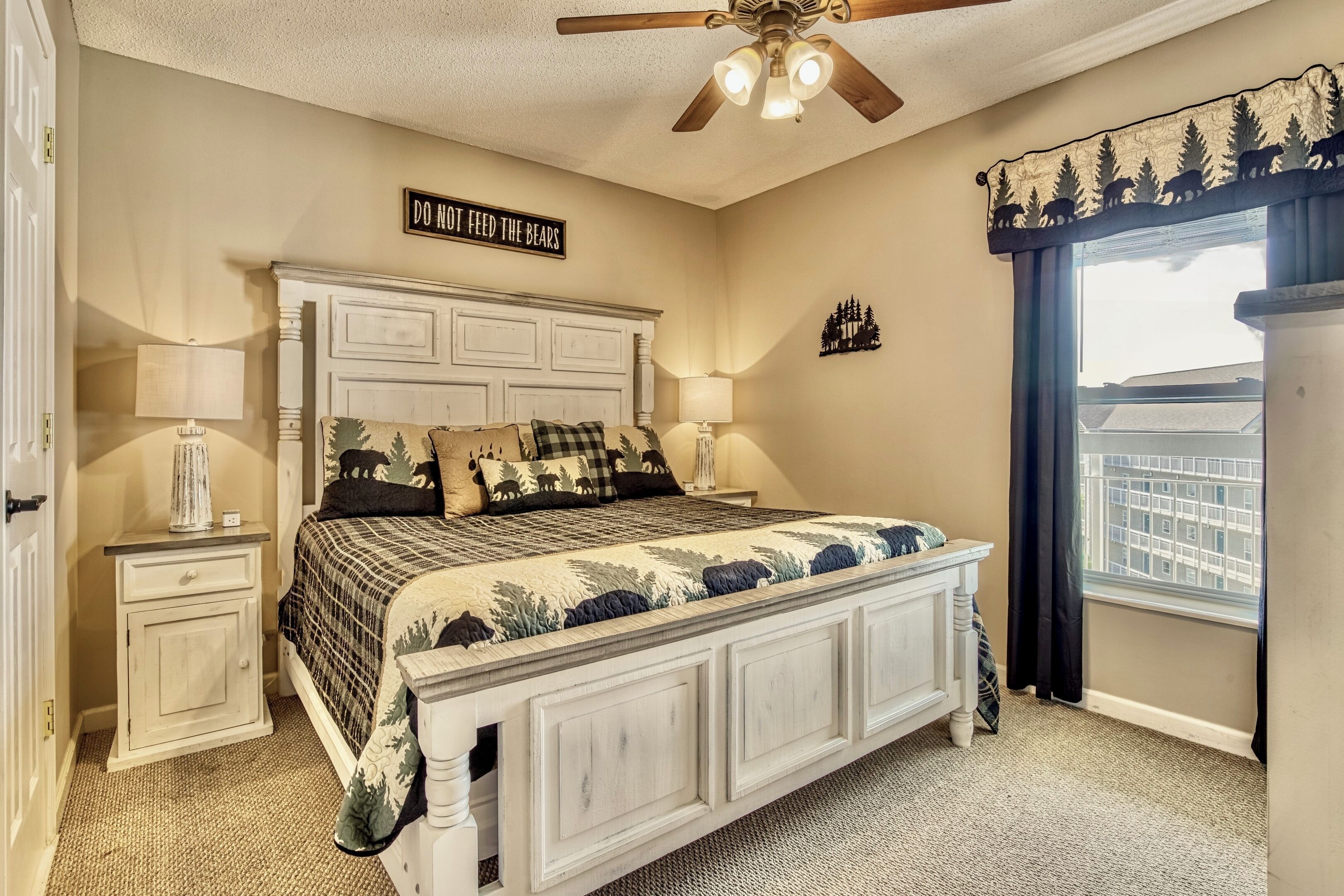 A bedroom with a bed, nightstands, a ceiling fan, a window with curtains, and a sign on the wall.