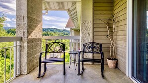 Ein Balkon mit zwei schwarzen Metallstühlen und einem kleinen runden Tisch, mit Blick auf eine üppige grüne Landschaft mit Hügeln.
