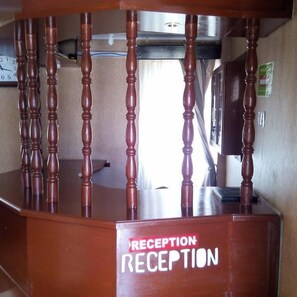 A reception desk with a sign that reads "RECEPTION" and a wooden railing. - Tripple T Hotel (Luanda)