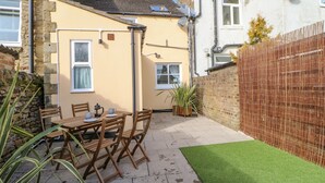 A patio with a table and chairs, a small garden, and a brick wall. - Elm Cottage (Bishop Auckland)