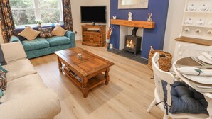 A living room with a sofa, a coffee table, a TV, a fireplace, and a dining area. - Elm Cottage (Bishop Auckland)