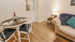 A dining area with a table set for two, a sofa, a lamp, and a door with decorative glass panels. - Elm Cottage (Bishop Auckland)