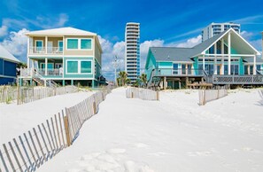 A beachfront property with a sandy walkway, a tall building, and a two-story house with a balcony. - Lagoon Tower 302, 3/3 | Private Beach Access (Gulf Shores)