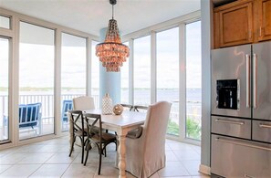 A dining area with a table and chairs, a chandelier, and a view of the sea through large windows. - Lagoon Tower 302, 3/3 | Private Beach Access (Gulf Shores)
