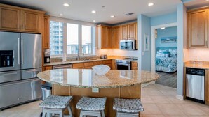 Una cocina moderna con encimeras de granito, electrodomésticos de acero inoxidable, armarios de madera y una isla grande con taburetes.