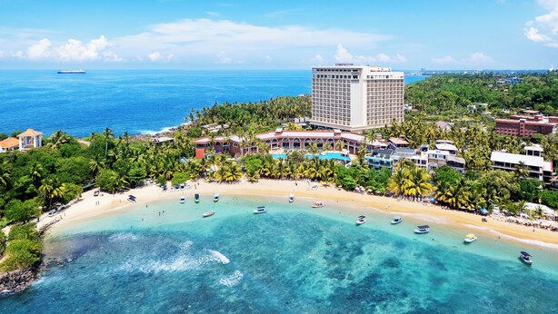 Vista aérea de un complejo turístico costero con playa, aguas turquesas cristalinas y un gran edificio de hotel.