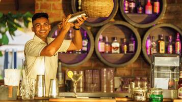 A bartender preparing a drink at a bar with wine barrels in the background.