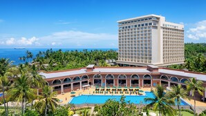 Un hotel con una piscina grande, palmeras y vista al océano.