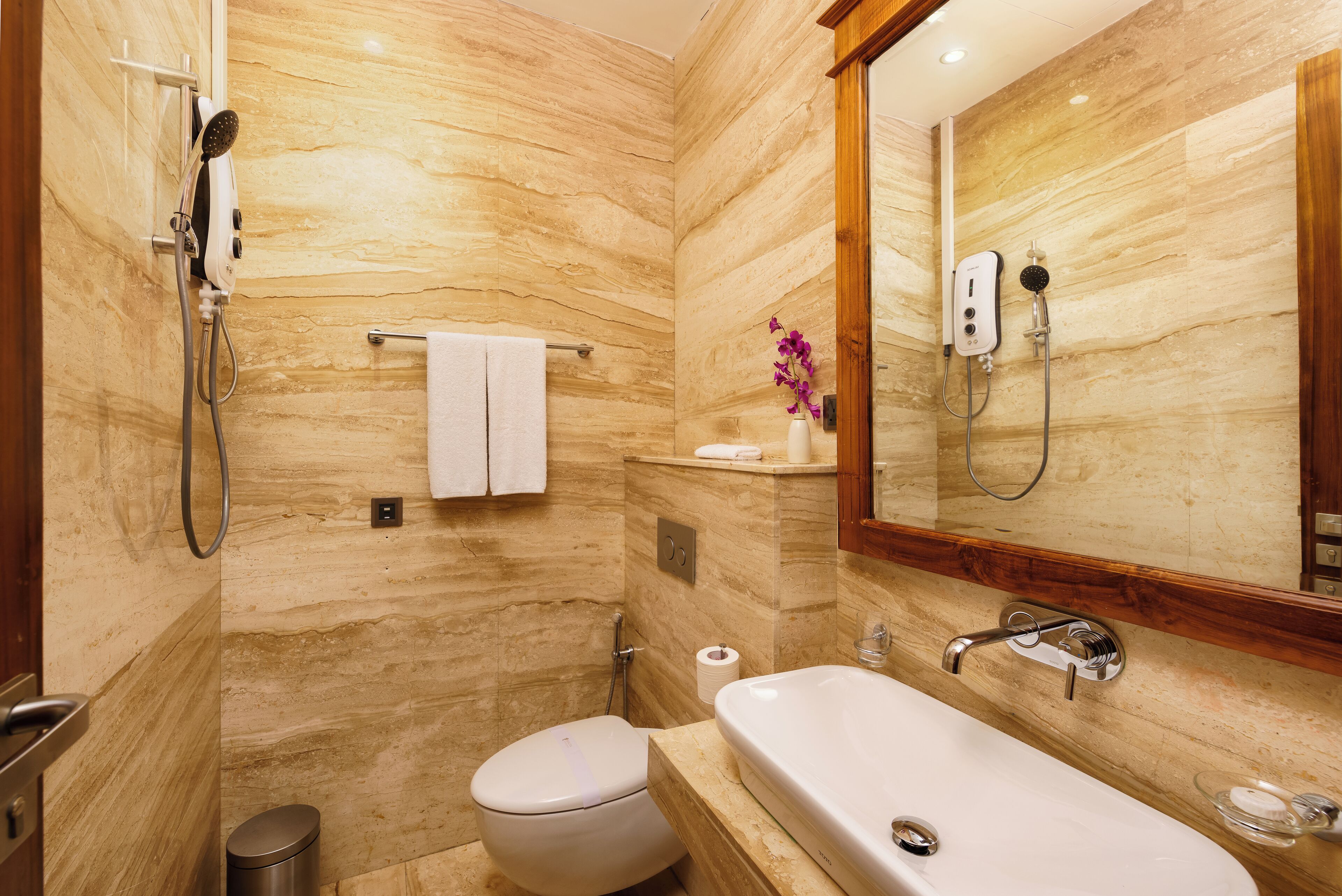 A bathroom with a marble wall, a toilet, a sink, and a shower.