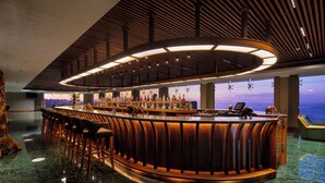 Un bar con un diseño de madera curvada, un techo alto con listones de madera y vistas de la ciudad a través de grandes ventanales.