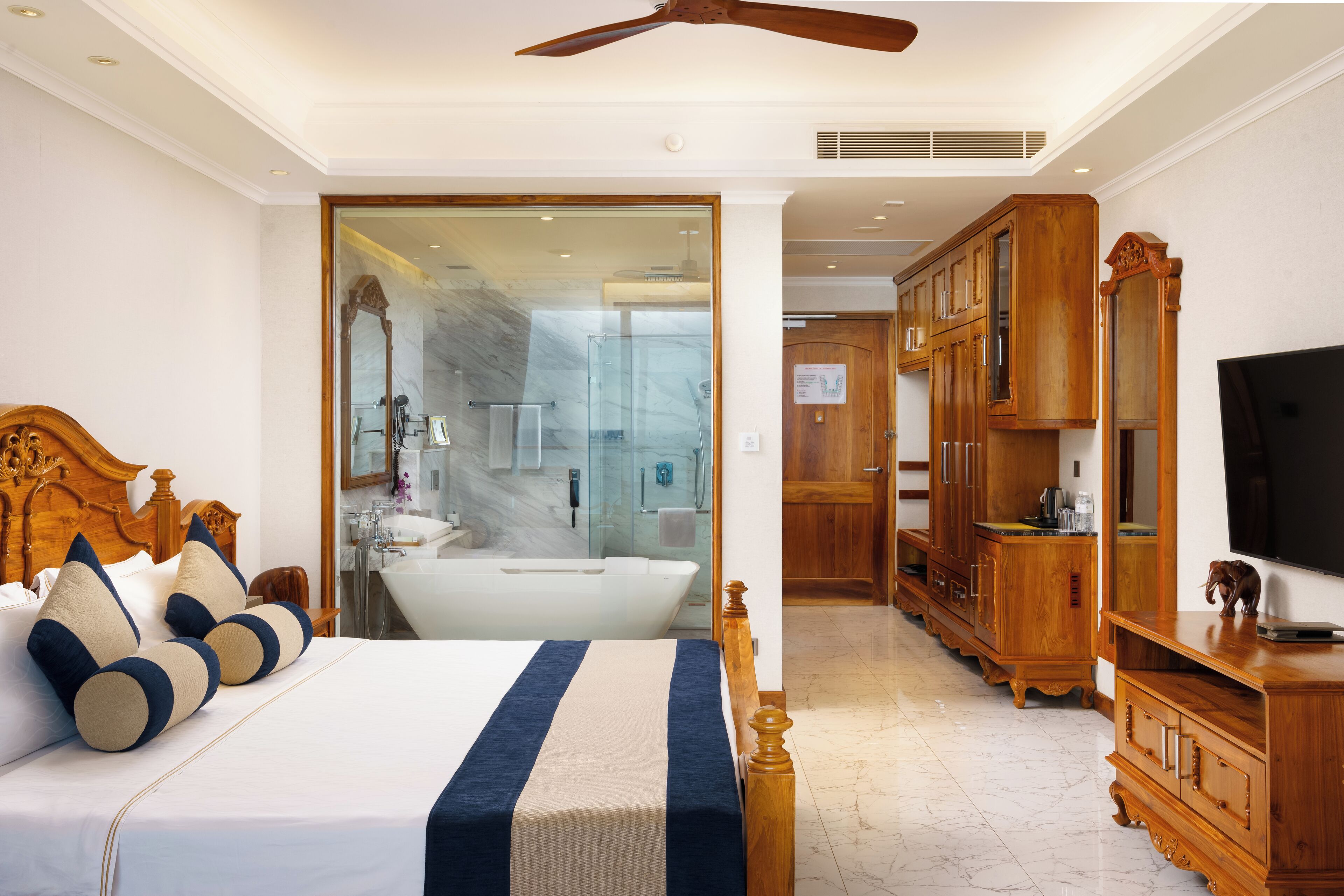 A hotel room with a large bed, wooden headboard, a wooden wardrobe, a television, and a bathroom with a bathtub and shower.