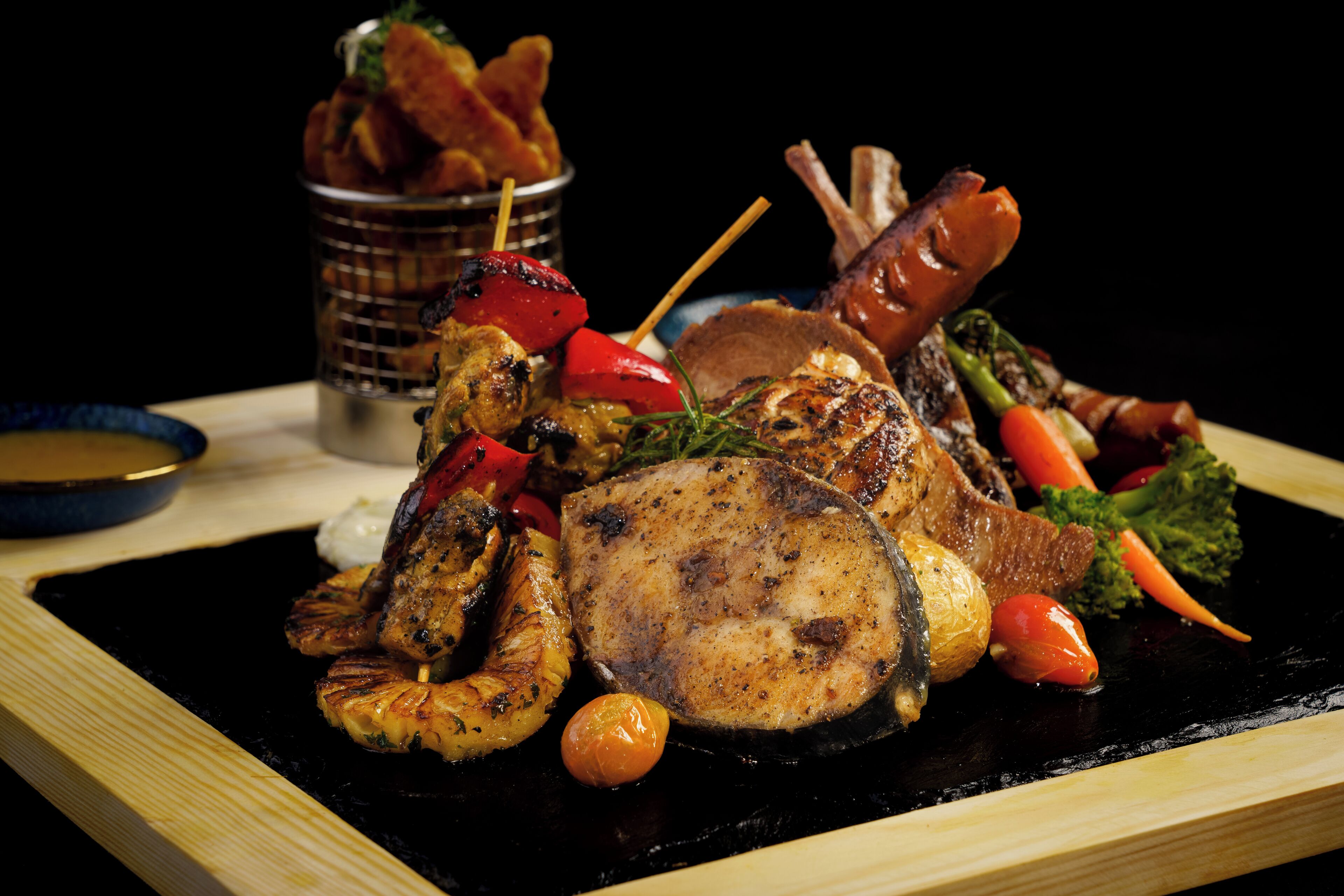 A variety of grilled meats and vegetables on a black plate.