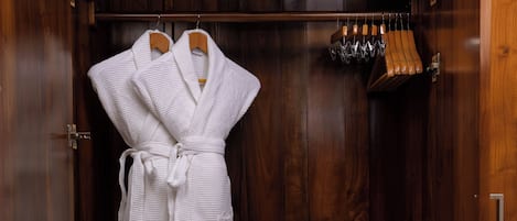 A wooden wardrobe with a robe hanging inside, a black safe, and a set of wine glasses on the top shelf.