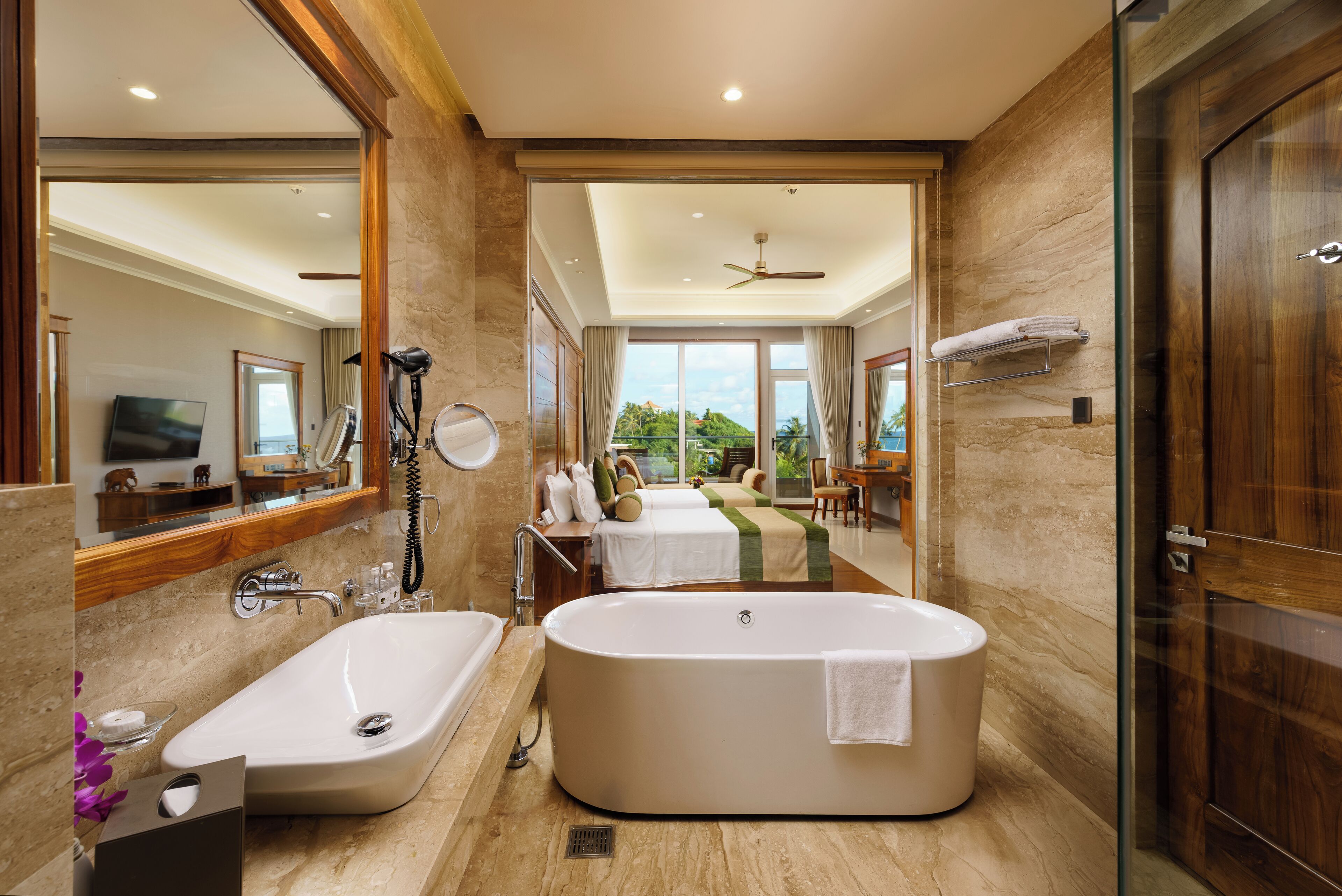 A modern bathroom with a large bathtub, a separate sink, and a shower area. There is a large mirror, a vanity with a mirror, and a window providing a view of the outdoors.