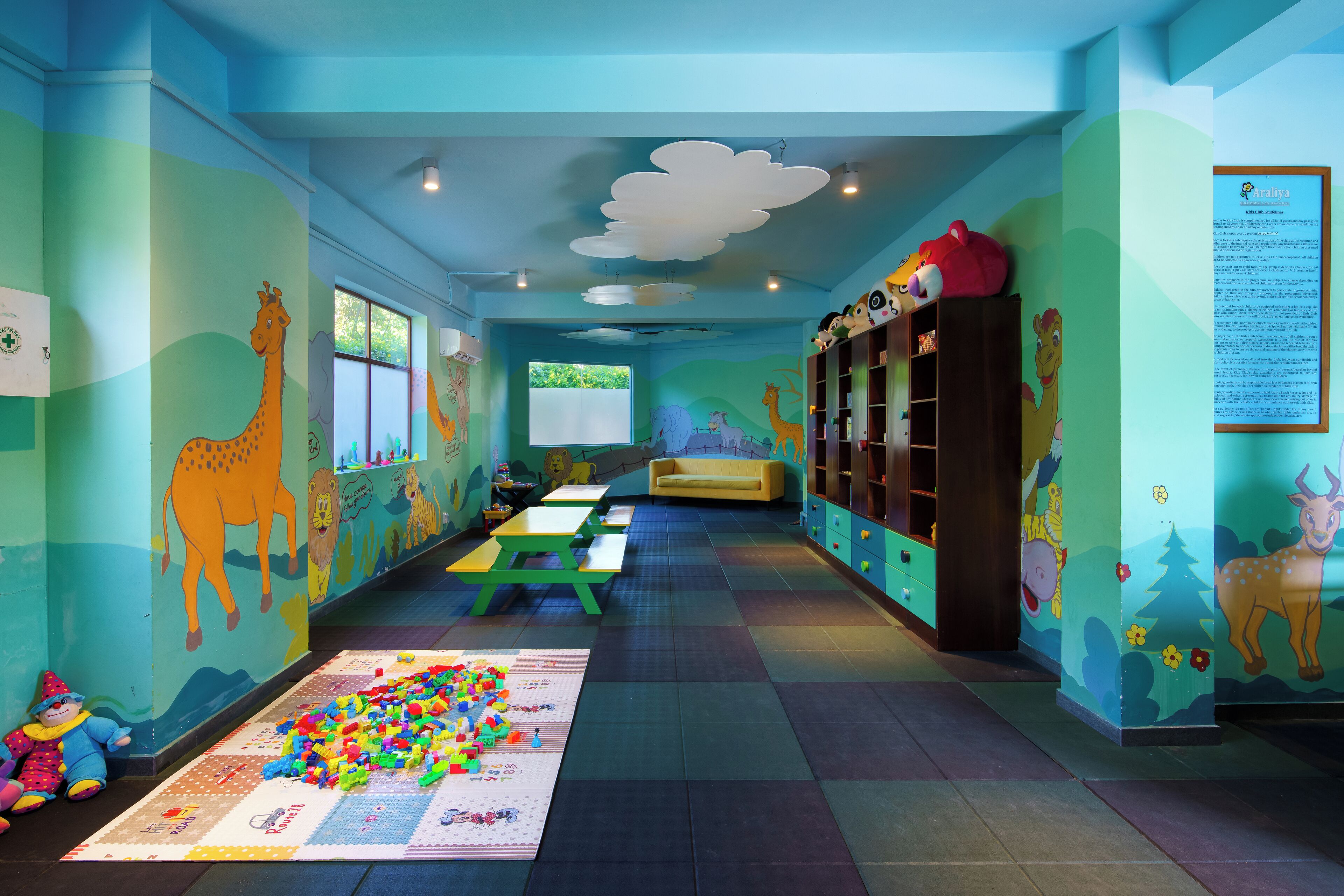 A children's playroom with colorful murals, play tables, and a large play mat.