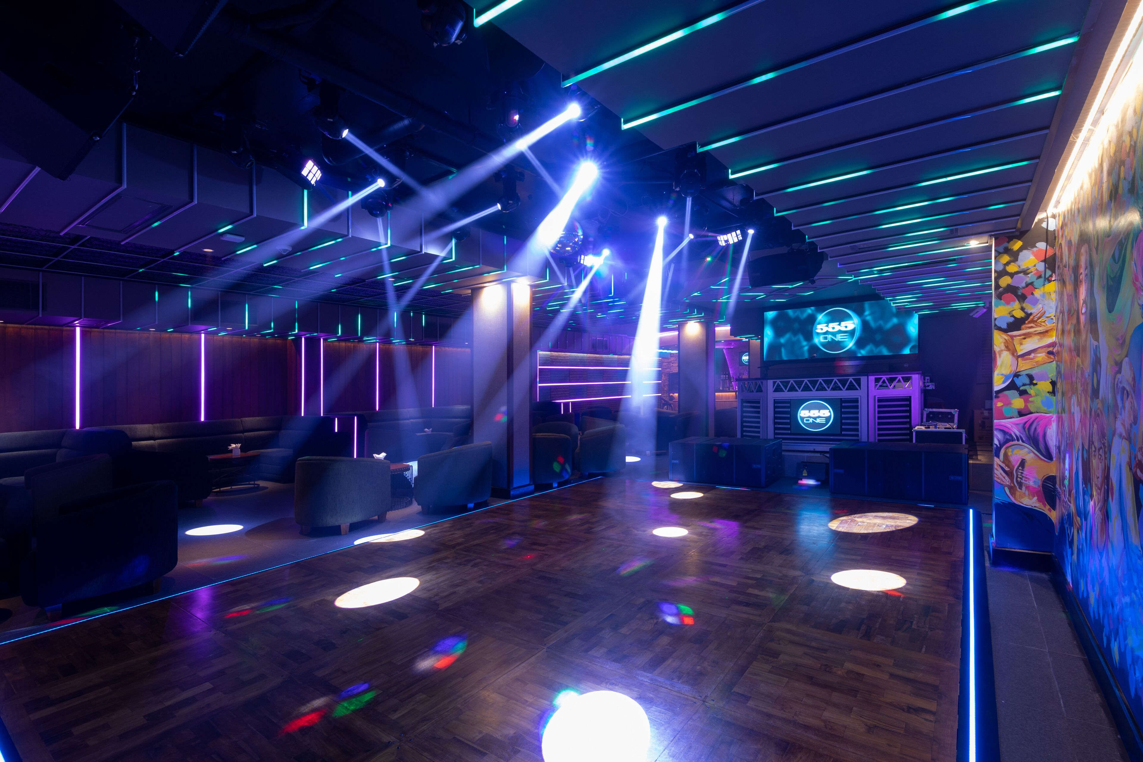 A modern lounge area with a wooden floor, ambient lighting, and a large screen displaying '888 ONE'.