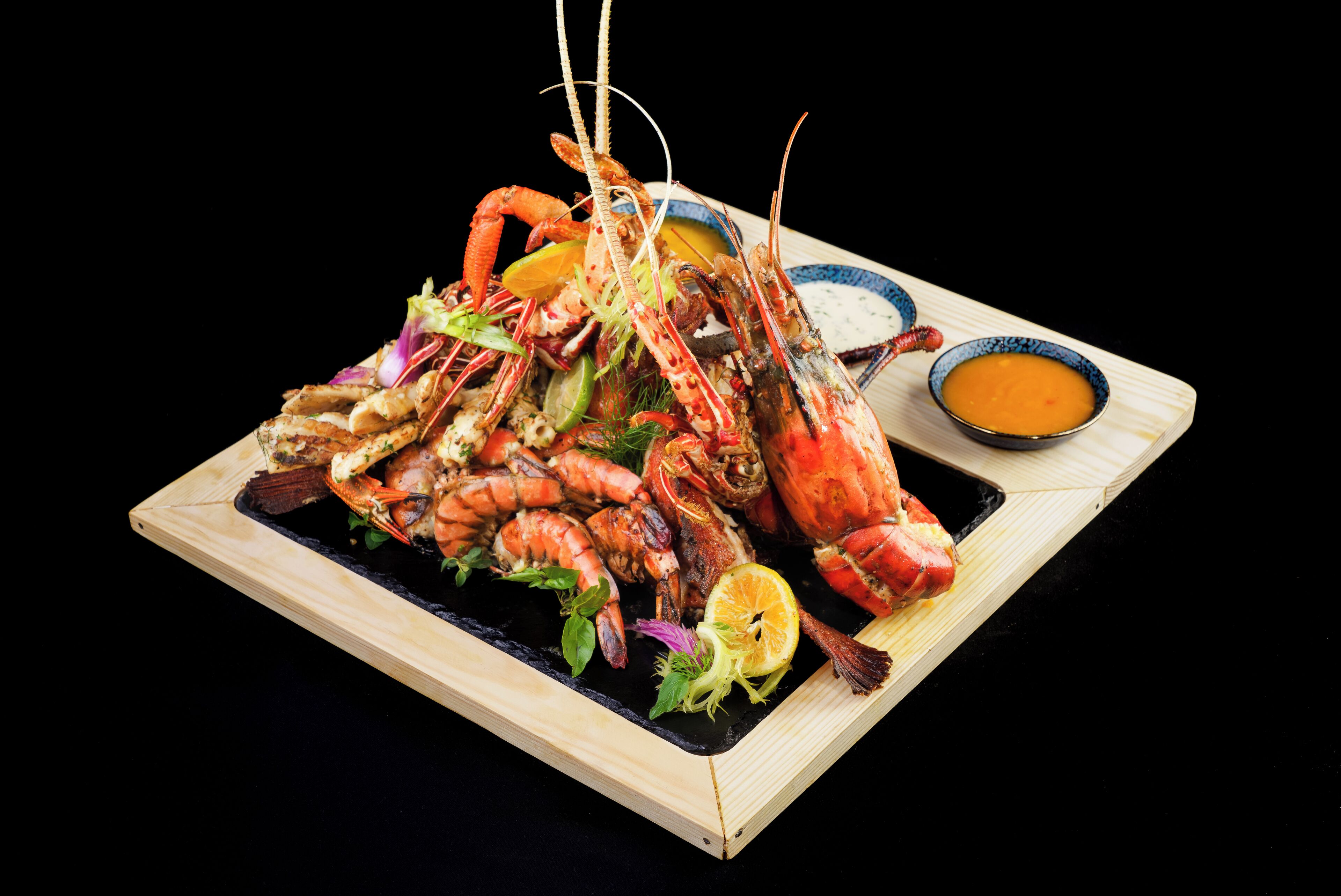 Un piatto di pesce con diversi tipi di crostacei e guarnizioni, accompagnato da una ciotola di salsa.