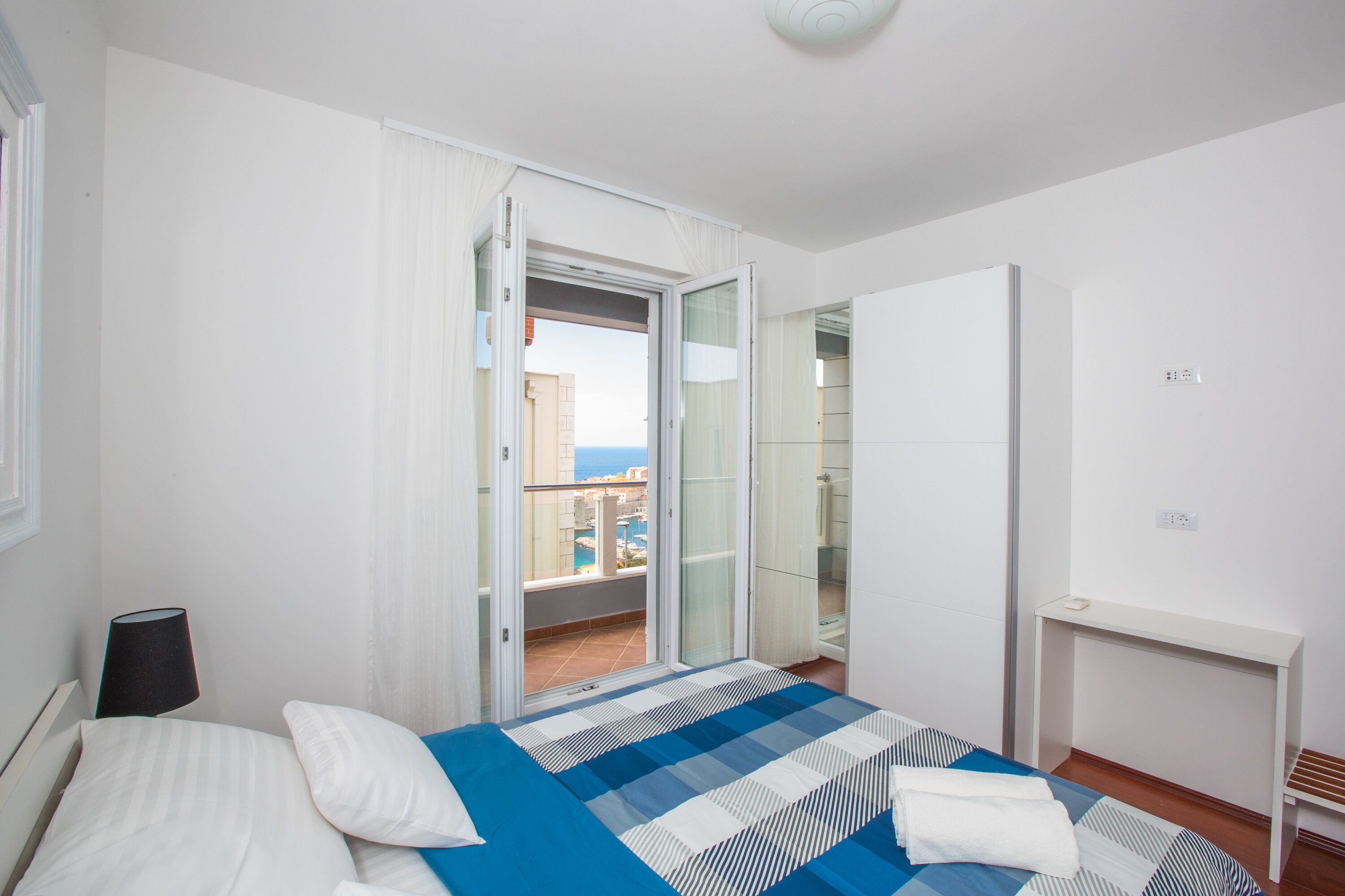 Habitación de hotel con cama, mesita de noche, escritorio y vistas al balcón exterior.