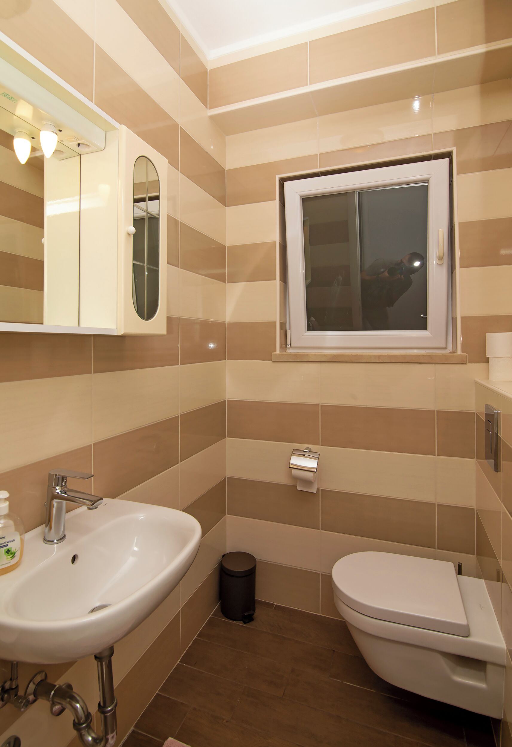 Une salle de bain avec un lavabo blanc, des toilettes, un miroir et une fenêtre.