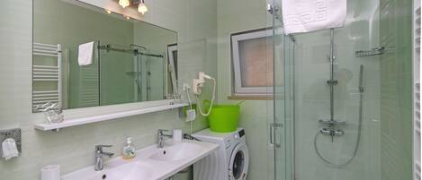 Ett modernt badrum med en dusch som är avskärmad med glasväggar, en inbyggd tvättmaskin och en stor spegel ovanför handfatet.