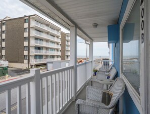 A balcony with wicker chairs and a small table, overlooking a building with multiple balconies.