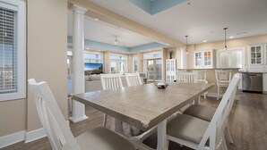 A spacious dining area with a large wooden table and white chairs, surrounded by white cabinetry and a view of the city. - Stunning ocean block condo with 5 bedrooms and 4 and 1/2 baths! (Ocean City)