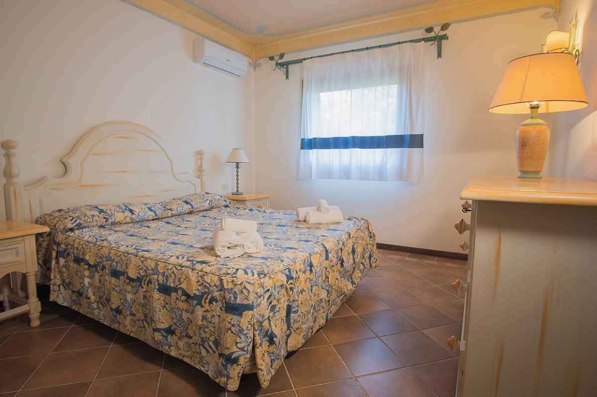 Un dormitorio con una cama, una mesita de noche, una lámpara y una ventana con cortinas.
