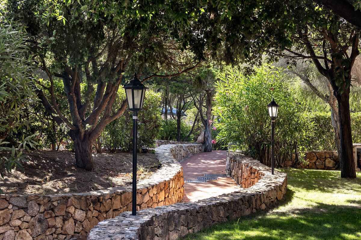 Ein gepflasterter Weg schlängelt sich durch einen Garten mit Bäumen und zwei schwarzen Laternen.