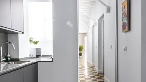 A modern kitchen with a sink, a microwave, and a plant. A hallway with a checkered floor leads to another room.