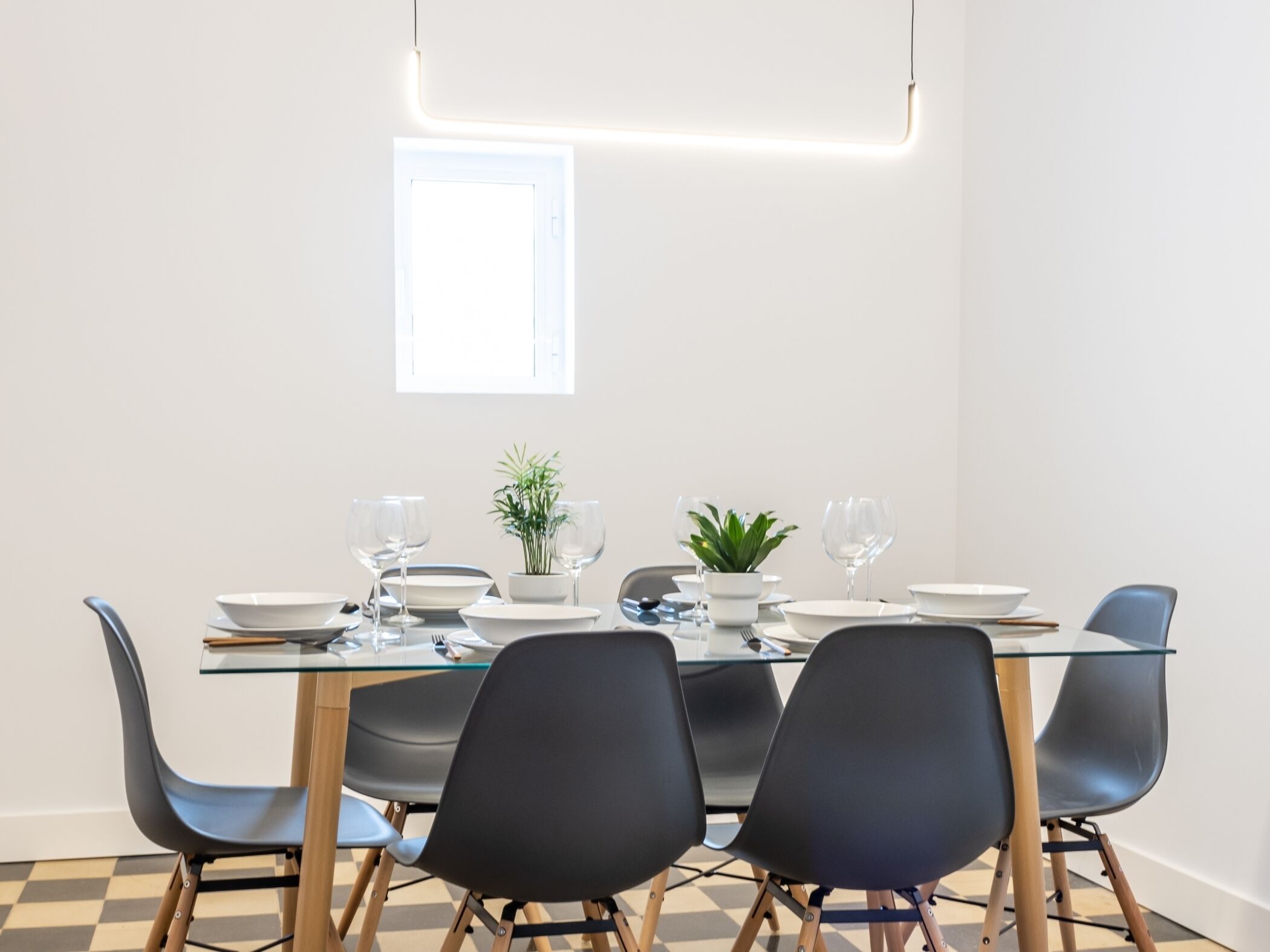 A modern dining area with a glass table, black chairs, and a small potted plant.