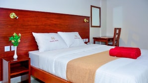 A hotel room with a wooden headboard, white bedding, a red towel, and a small bedside table with a vase of flowers. - Ndanga International (Ruiru)