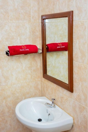 A bathroom with a white sink, a mirror with a wooden frame, and two red towels hanging on a towel rack. - Ndanga International (Ruiru)
