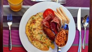 A breakfast plate with toast, bacon, beans, and a fried egg on a table with a striped placemat. - Ndanga International (Ruiru)