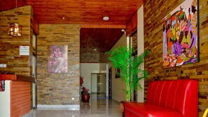 A lobby with a red sofa, a reception desk, a large plant, and a colorful mural on the wall. - Ndanga International (Ruiru)