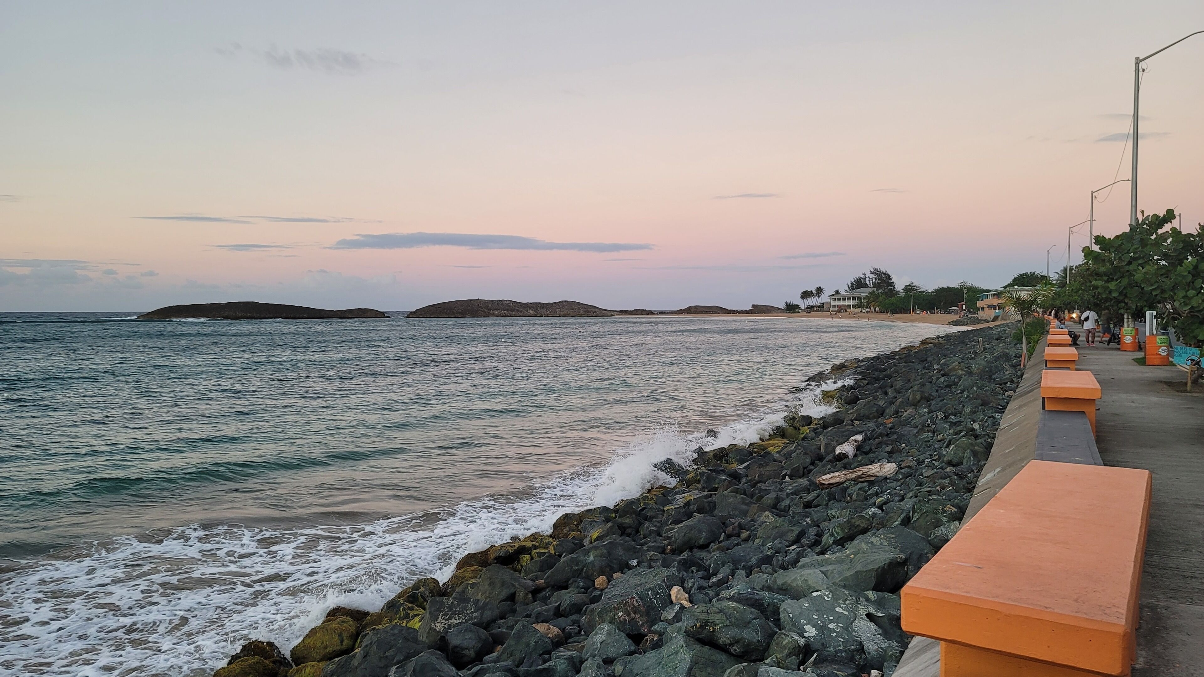 A coastal walkway with benches and a rocky shoreline.