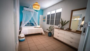 A bedroom with a bed under a white canopy, a bedside table with a vase, and a dresser. - Aguasalá Beach House, Puerto Nuevo Beach (Vega Baja)
