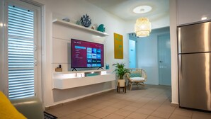 A modern kitchen with a built-in TV, a refrigerator, and a dining area with a chair and plant. - Aguasalá Beach House, Puerto Nuevo Beach (Vega Baja)