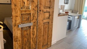A wooden door with a rustic design, a white wall with a framed picture, and a modern kitchen area with a dining table and chairs. - Albufeira Beach Apartment (Guia)