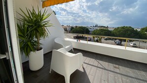 A balcony with a potted plant, white chairs, and a view of the cityscape. - Albufeira Beach Apartment (Guia)