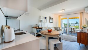 A modern kitchen with a built-in oven, a dining area with a round wooden table, and a balcony with a view of the city. - Albufeira Beach Apartment (Guia)