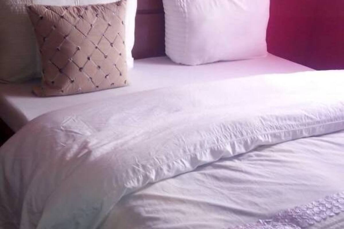 A bed with a white duvet, a beige quilted pillow, and a white pillow.