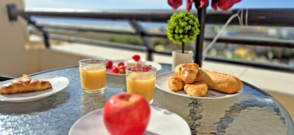 A table with croissants, juice, and an apple, with a balcony view in the background. - BUENA VISTA (Palm Garden) Apartment in Morro Jable, ocean view, pool (Morro Jable)