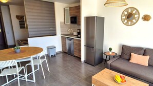 A modern kitchen with a refrigerator, dining table, and chairs. There is a sofa with cushions and a small table with fruit. - Apartment BUENA VISTA (Palm Garden) Morro Jable, sea view, pool (Morro Jable)