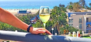 A balcony with a glass of white wine, overlooking a beach with palm trees and a clear blue sky. - BUENA VISTA (Palm Garden) Apartment in Morro Jable, ocean view, pool (Morro Jable)