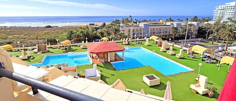 A resort with multiple swimming pools, a beach view, and palm trees.