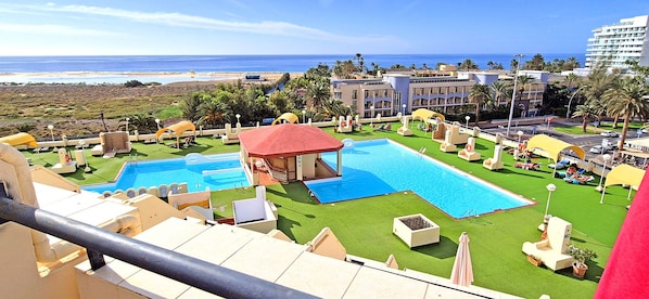 A resort with multiple swimming pools, a beach view, and palm trees.