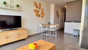 A modern living room with a flat-screen TV on a wooden cabinet, a dining area with a table and chairs, and decorative wall art. - Apartment BUENA VISTA (Palm Garden) Morro Jable, sea view, pool (Morro Jable)