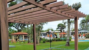 A covered outdoor area with a playground, a swimming pool, and a building with a red roof.